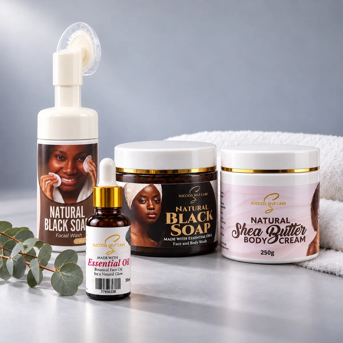 The Success Self Care line: foaming facial wash, essential oil blend, black soap, and shea butter body cream with a white towel and eucalyptus
